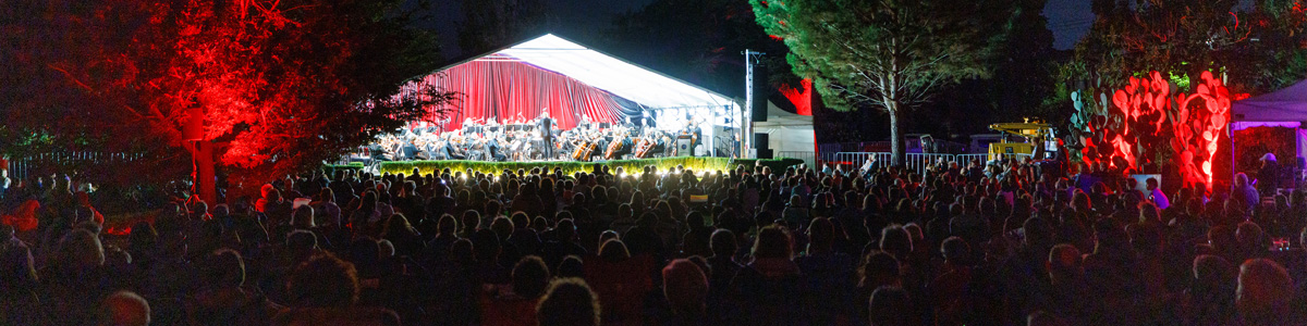 Evening crowd watching orchestra on stage in a park