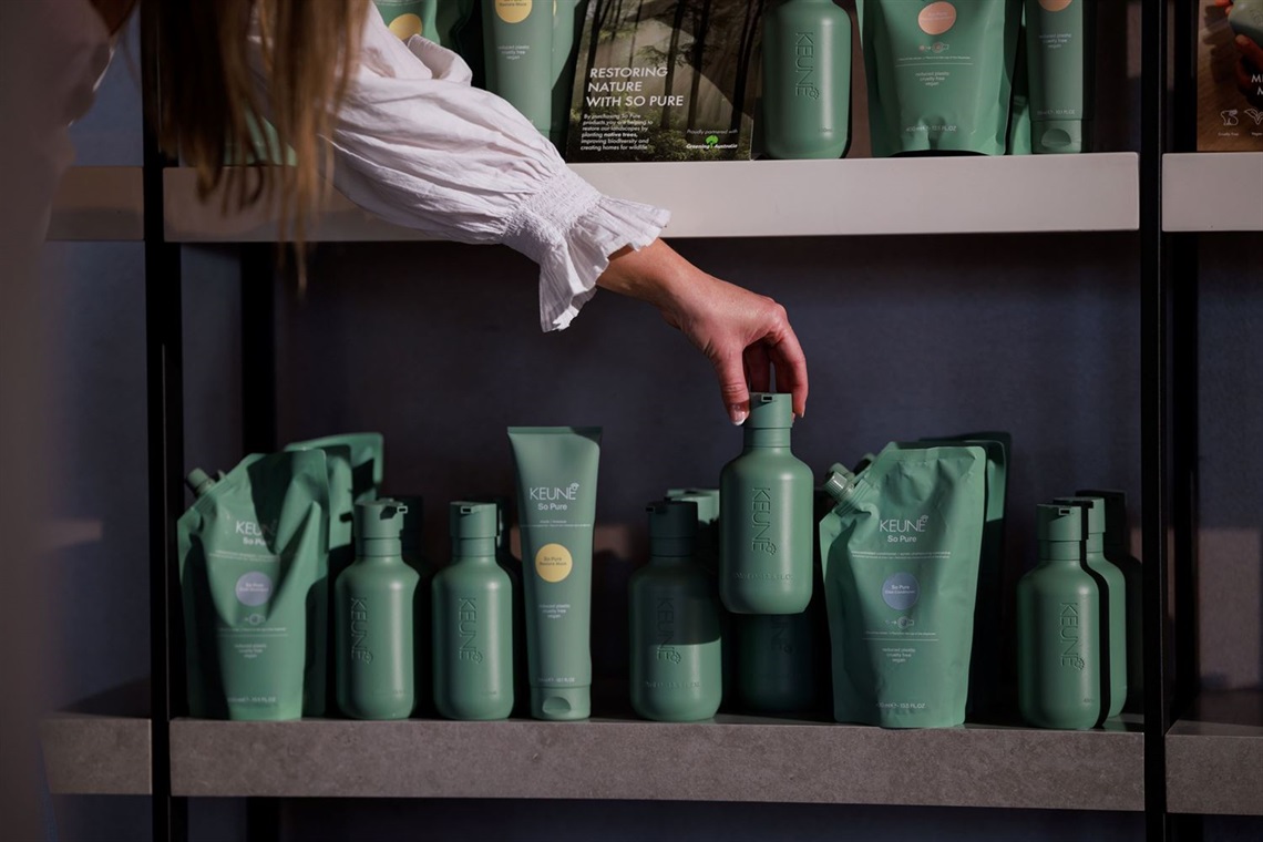 A hand is reaching down to select a bottle from a shelf full of hair products.