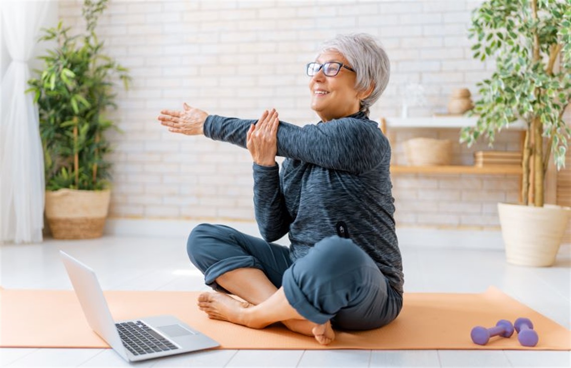 Older woman stretching in front of laptop before fitness class